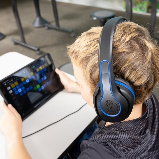 Child using TWT Audio's REVO noise-reducing headphones while working on a tablet in a classroom setting.